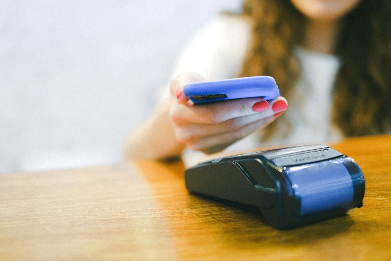 Close-up of a woman making a contactless payment using a smartphone over a card reader