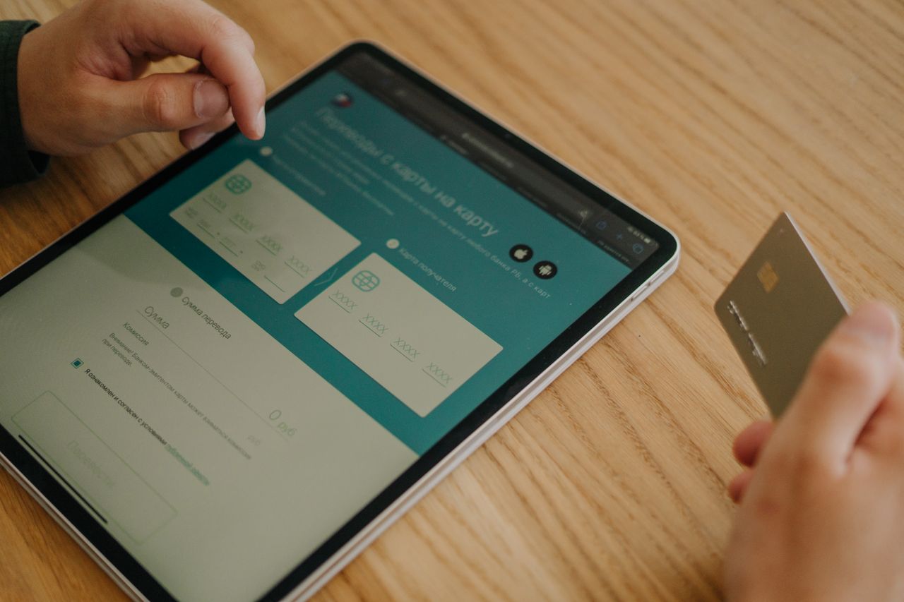 Services Hands making an online purchase using a tablet and credit card on a wooden table.
