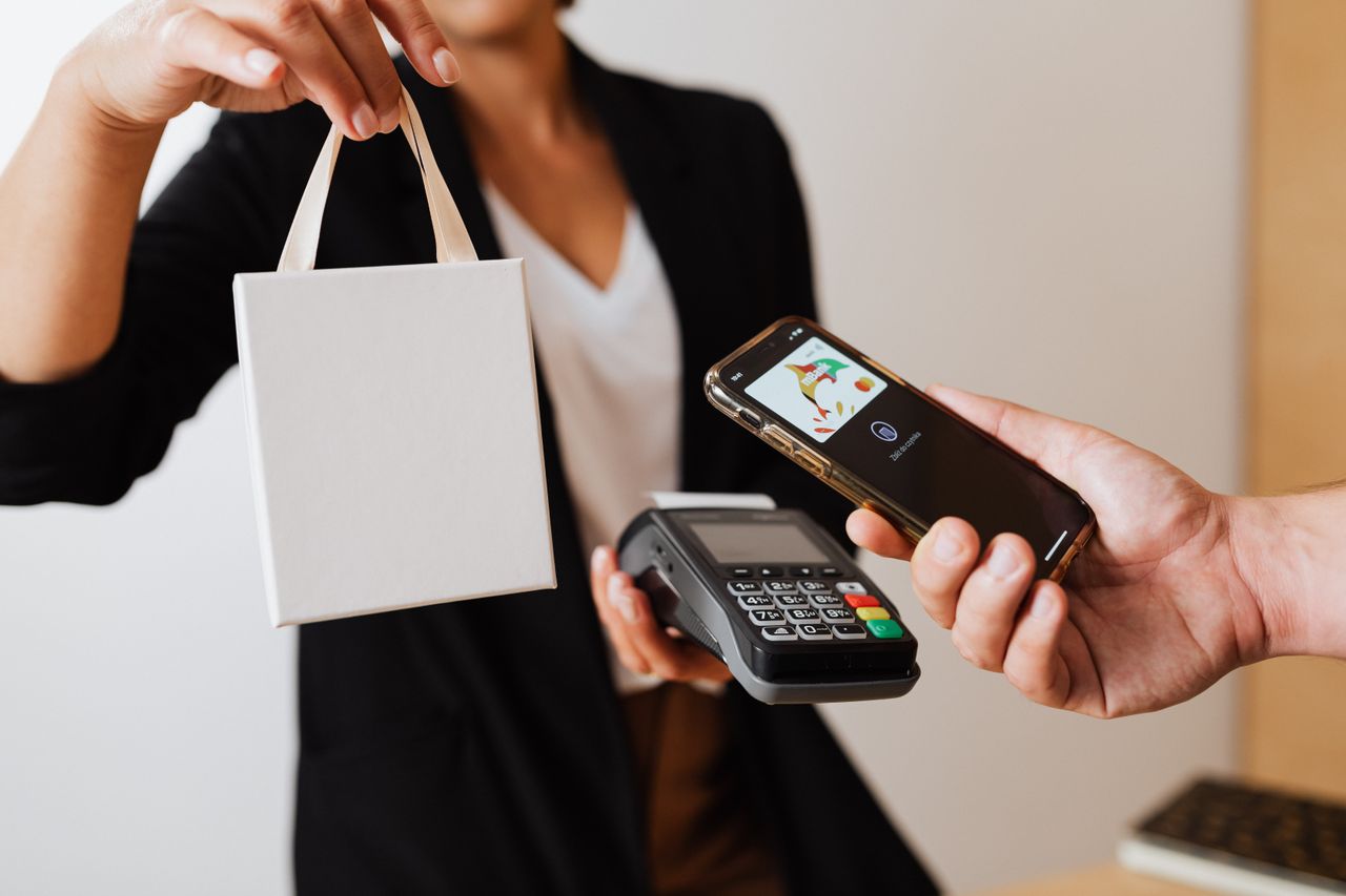 Services A person uses a smartphone for contactless payment with a payment terminal, while receiving a shopping bag.