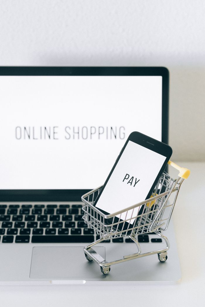 A smartphone in a miniature cart on a laptop symbolizes online shopping and digital payment.