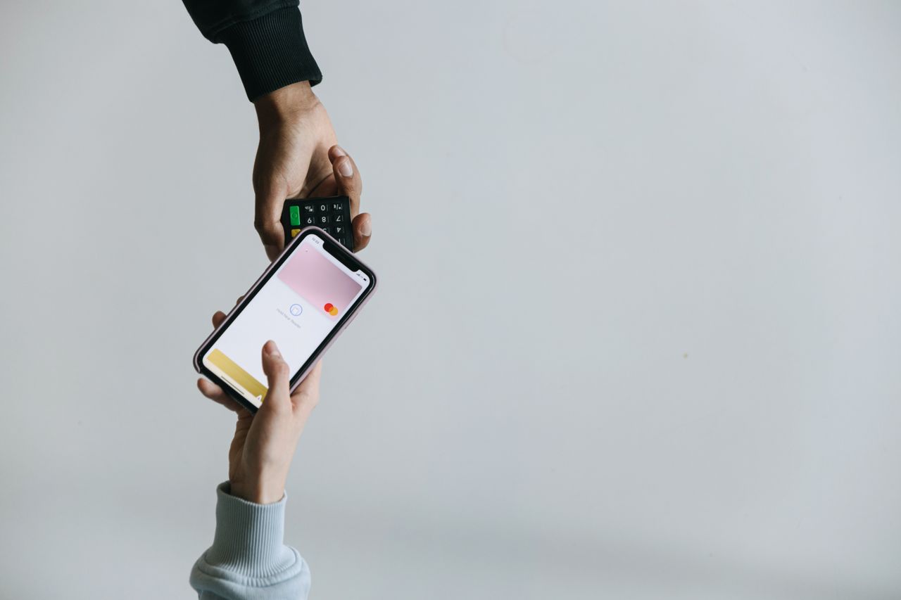 Hands using smartphone and terminal for cashless payment, showcasing modern transaction methods.